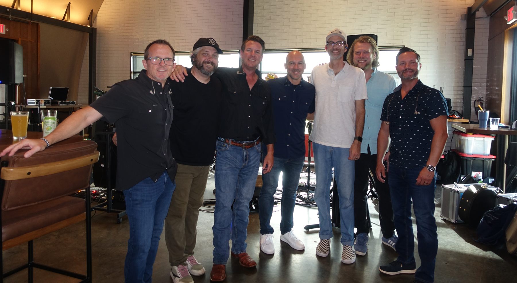 Seven members of Turnberry Jam posing together, arms around each other, in front of their gear after a show.