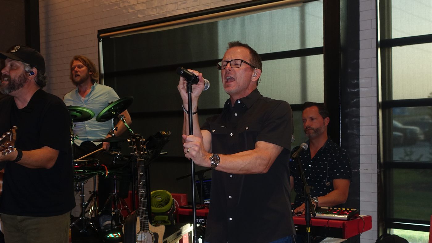 Singer belting into the mic, with the drummer and keyboard player behind him.