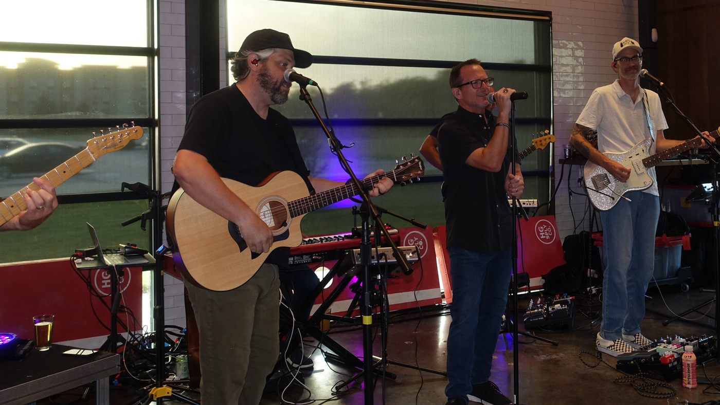 Acoustic guitarist, singer and electric guitarist singing together at an indoor show.