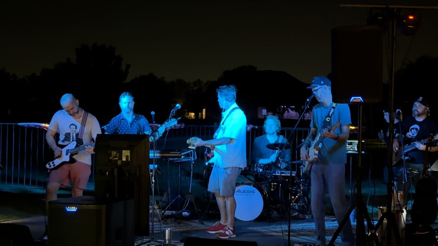 The band under blue stage lights at a backyard show.